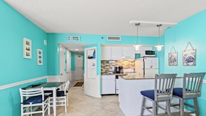 Una cocina con gabinetes blancos, microondas y cafetera. Hay una mesa de comedor con sillas y un letrero que dice "Baker House".
