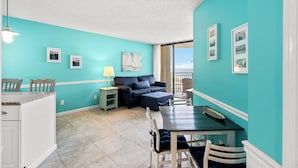 Un espacio habitable pequeño con paredes verde azulado, una zona de comedor, un sofá y un balcón con vistas.