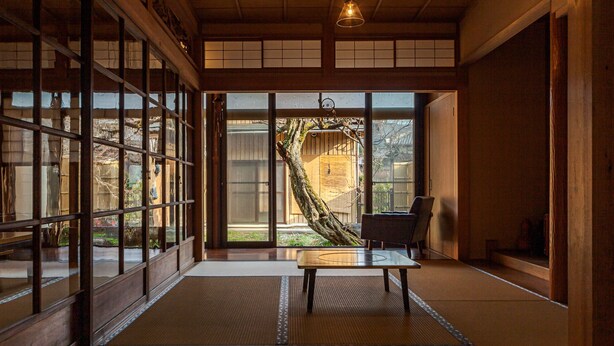 Ein traditioneller japanischer Raum mit Tatami-Böden, Schiebetüren und Blick auf einen Garten.