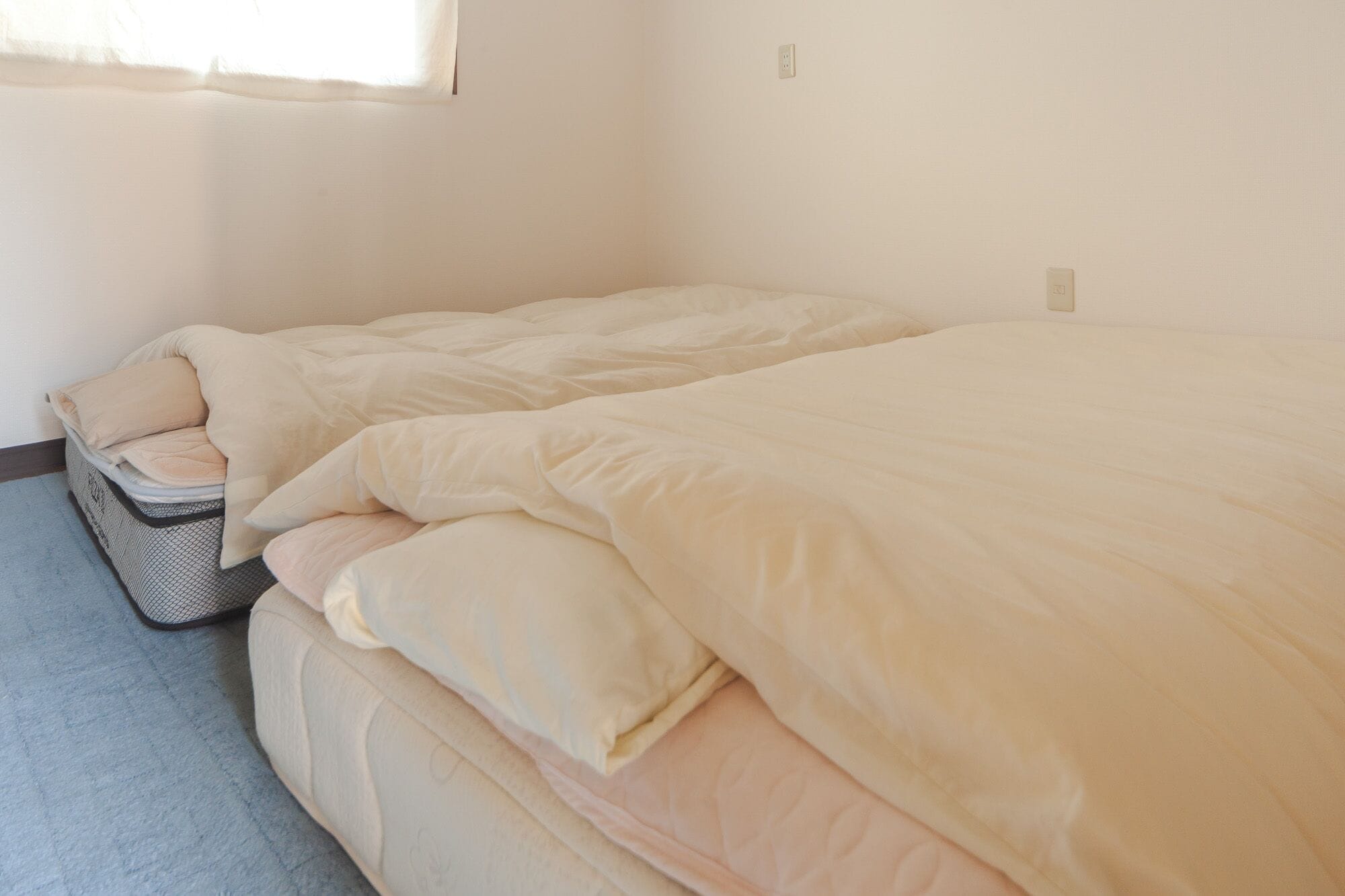 Une chambre avec deux lits, une petite fenêtre et une prise de courant au mur.