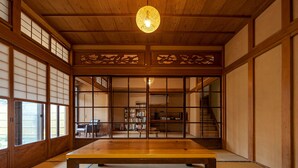 Ein traditioneller japanischer Raum mit Tatami-Böden, einem niedrigen Tisch, Schiebetüren und einer hängenden Leuchte.