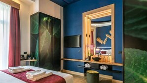 A hotel room with a bed, a TV, a mirror, a vanity with a sink, and a wooden cabinet. - Artion City Boutique Hotel (Heraklion)