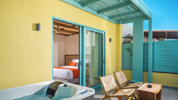A room with a hot tub, two wicker chairs, a wooden table, and a bed with orange bedding. - Artion City Boutique Hotel (Heraklion)