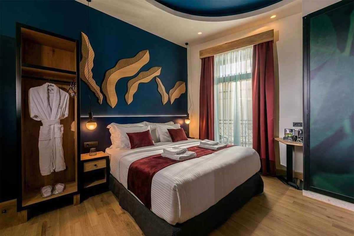 A hotel room with a large bed, a wardrobe, a vanity with a mirror, and a large window with curtains.