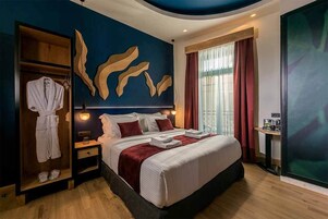Quarto de hotel com uma cama grande, um guarda-roupa, uma cômoda com espelho e uma janela ampla com cortinas.