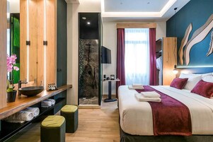 A modern hotel room with a large bed, a wooden vanity with a sink, a shower area, and a television.