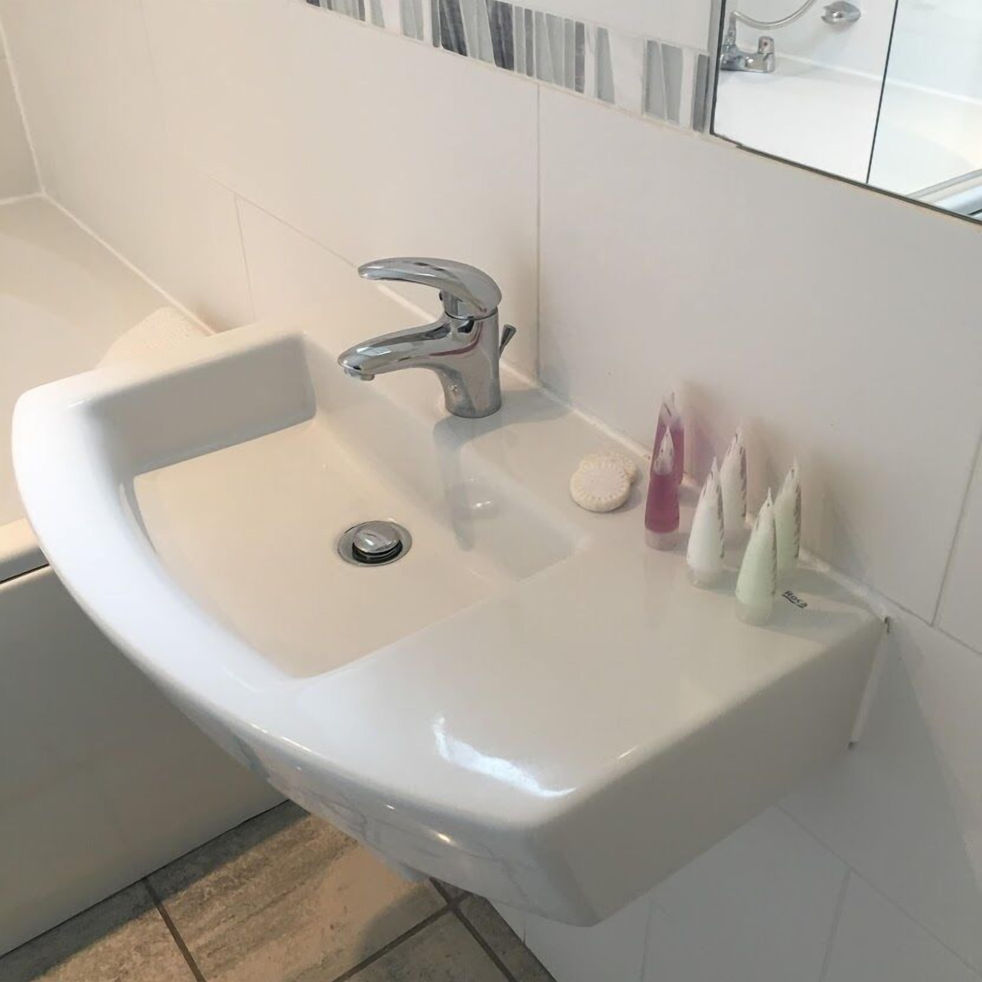 A white bathroom sink with a modern faucet, a mirror above it, and a few toiletries on the sink's edge.
