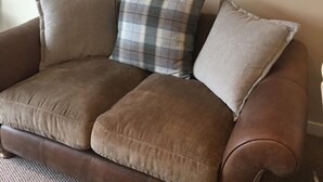 A brown leather sofa with three cushions, a plaid pillow, and a herringbone-patterned pillow. - Tay Pearls - Tay Chambers Apartment (Perth)
