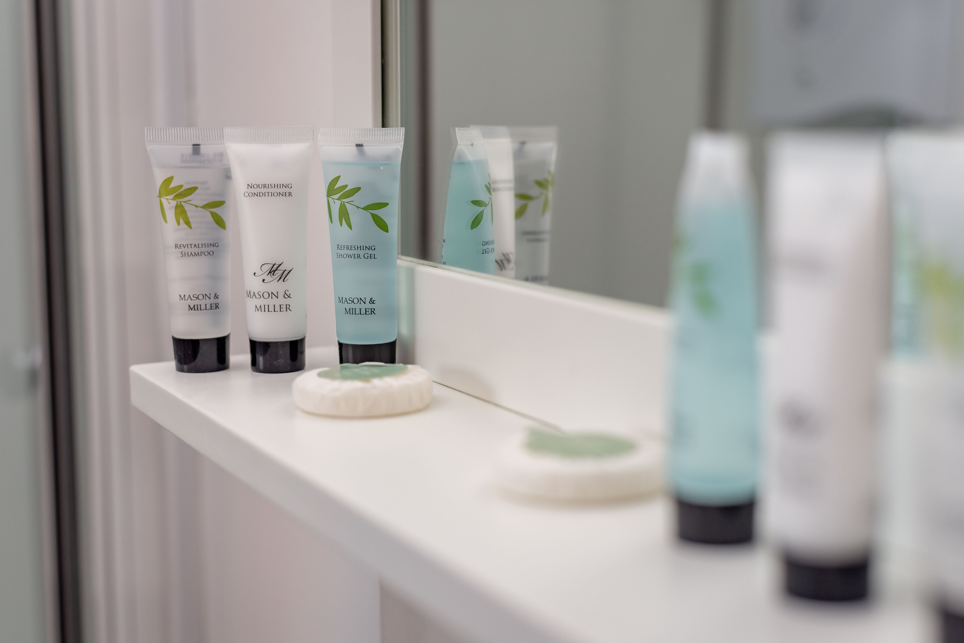 A bathroom shelf with various personal care products from Mason & Miller, including shampoo, conditioner, and body gel.