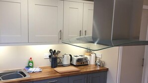 A modern kitchen with grey cabinets, a stainless steel range hood, a wooden countertop, and a black induction cooktop. - Tay Pearls - Tay Chambers Apartment (Perth)