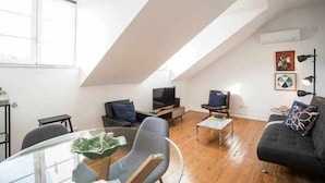 Een woonkamer in loftstijl met een schuine plafond, een glazen eettafel en een zwarte bank.