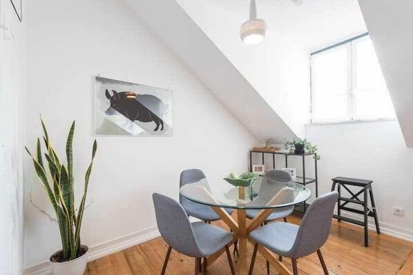 A dining area with a glass table and four chairs, a potted plant, and a framed artwork on the wall. - Excellent Location A/C and views in Principe Real (Lisboa)