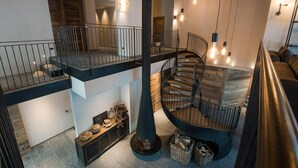 Interior moderno com escadaria em espiral, um banco de madeira com objetos decorativos e vista para o andar superior.