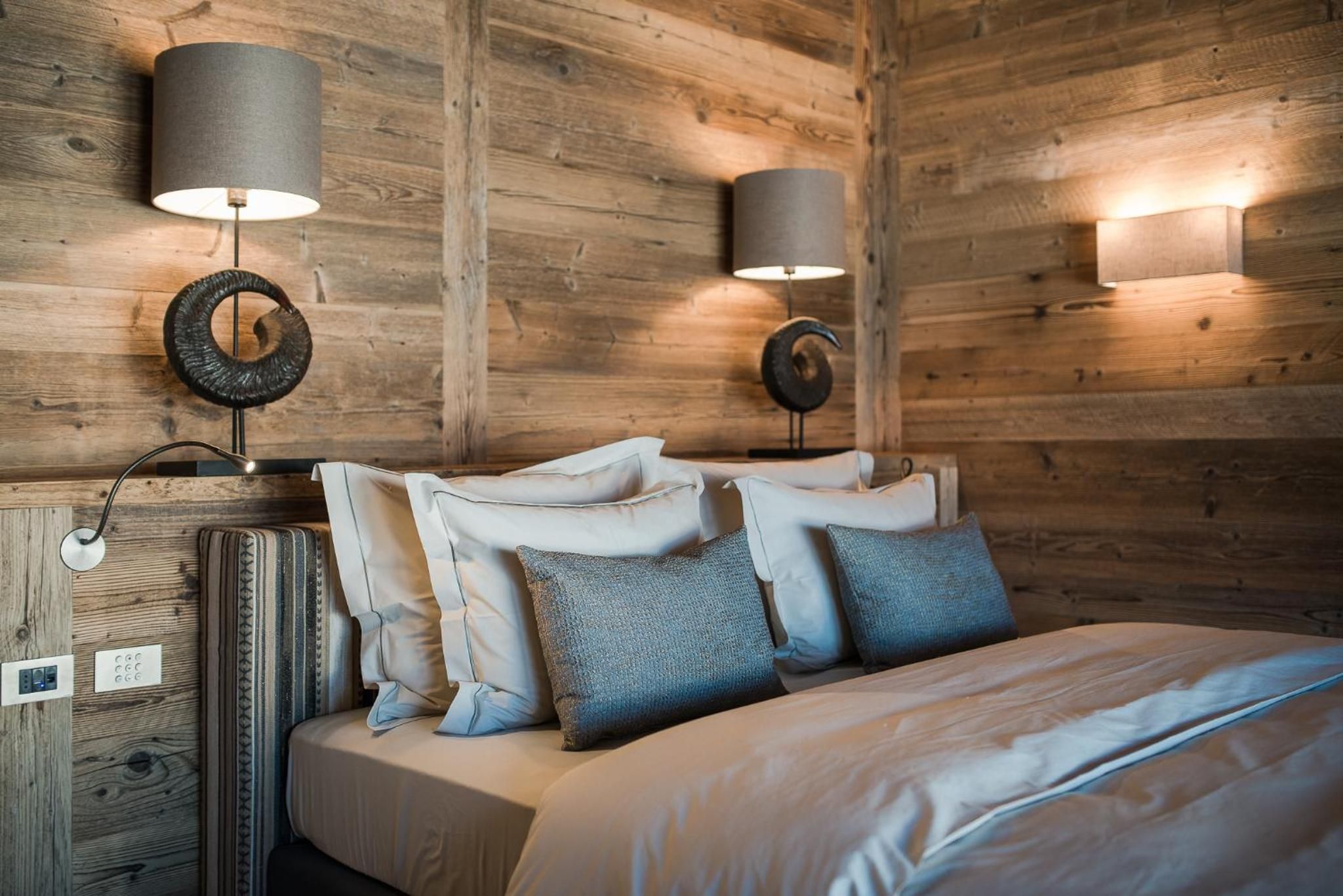 A wooden-paneled room with a bed, two wall-mounted lamps, and a circular wall decoration.