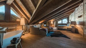 Um quarto de sótão espaçoso, com uma janela grande, uma banheira e um espaço de estar acolhedor.