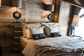 A wooden cabin-style bedroom with a bed, pillows, and two wall-mounted lamps. - Sunny Valley Mountain Lodge (Valfurva)