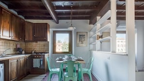 Une cuisine avec des meubles en bois, un pare-feu en carrelage, une table à manger avec des chaises et une fenêtre donnant sur des immeubles.