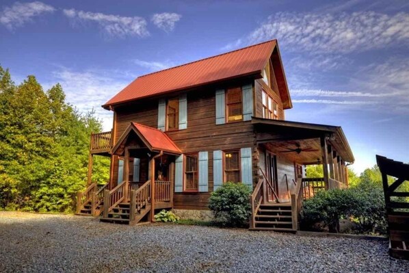 Une cabane en bois avec un toit rouge, une véranda et une allée gravillonnée.