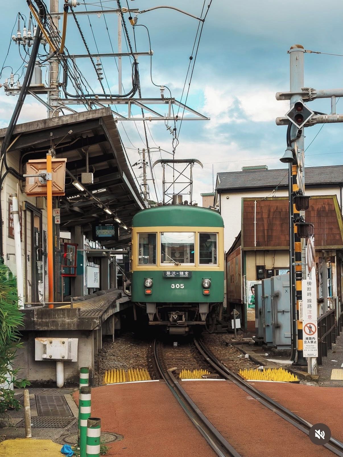Un tren verde y amarillo en una estación, con cables eléctricos aéreos y un andén.