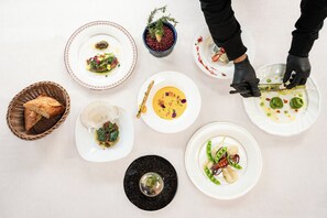 A top-down view of a dining table with various dishes, a small potted plant, and a basket of bread. - Casablanca Pool House (Kamakura)