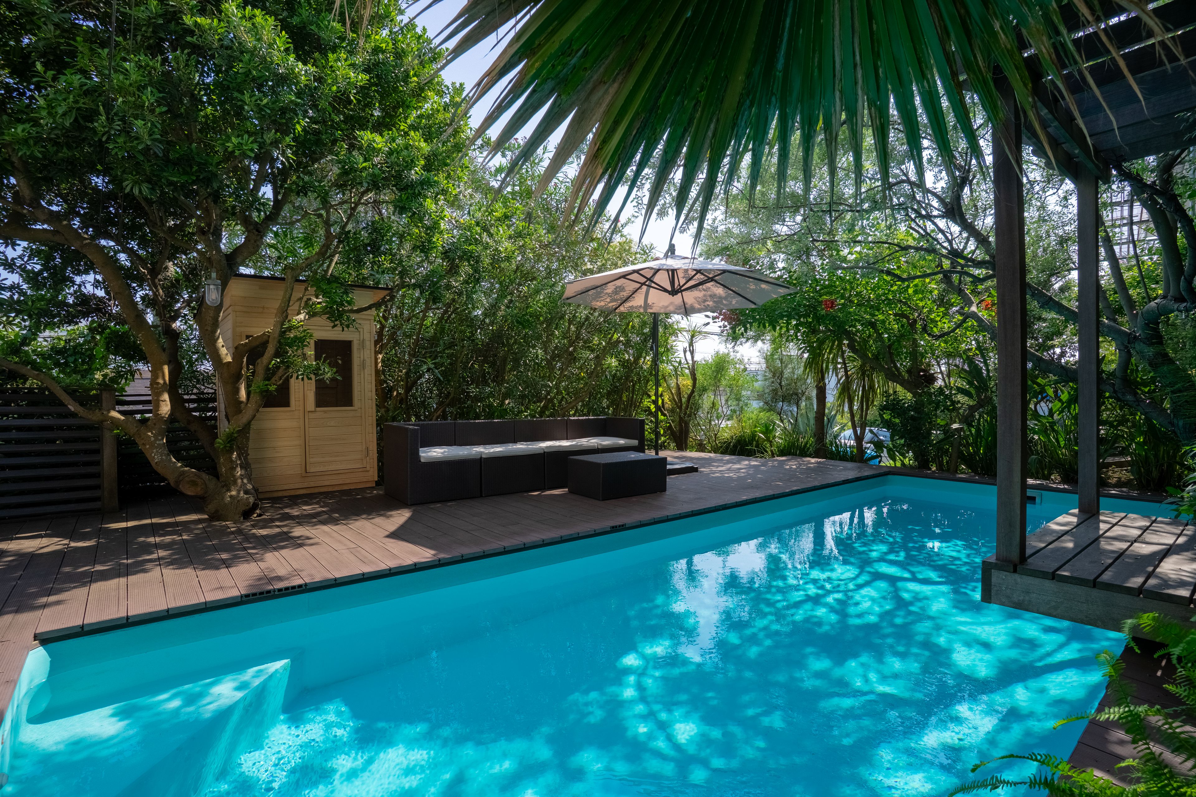A swimming pool with a wooden deck, a seating area, and a pergola with an umbrella.