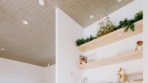 A modern, minimalistic bedroom with a wooden floor, white walls, and a bed with white bedding. There is a kitchenette with a microwave and a small refrigerator. - Casablanca Pool House (Kamakura)