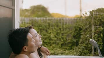 A couple relaxing in a hot tub with a view of greenery and a fence in the background.