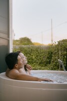 Una pareja relajándose en un jacuzzi con vistas a la vegetación y una valla al fondo.