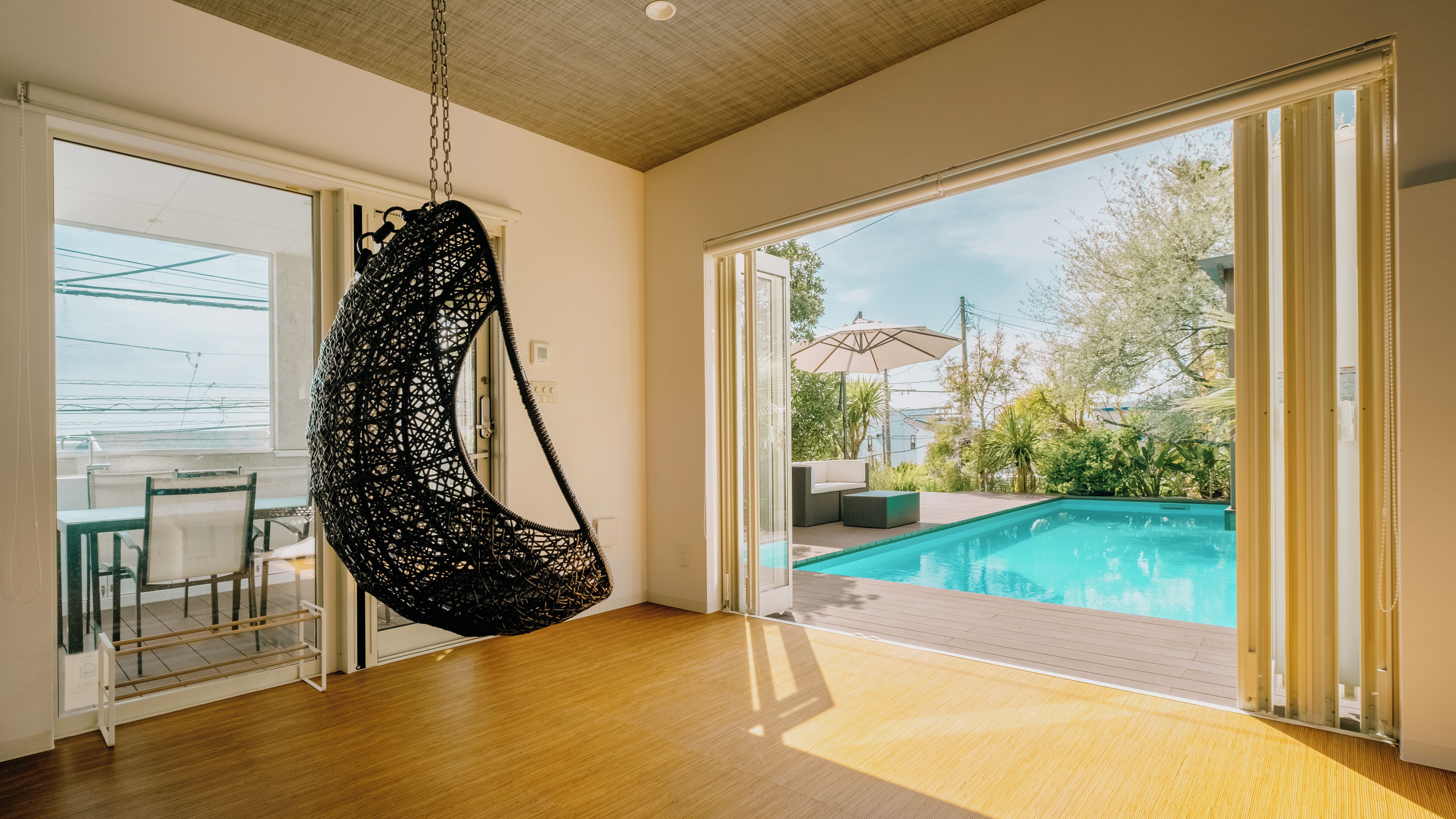 Ein Zimmer mit Hängekorbsessel, Schwimmbad und einer Glastür zum Außenbereich.