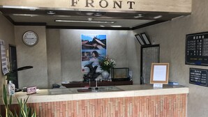 A hotel reception desk with a 'FRONT' sign above, a clock, a framed picture, a menu board, and a potted plant. - Business hotel route9 (Matsue)