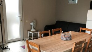 Un coin repas avec une table et des chaises en bois, un petit ventilateur blanc et un tableau encadré au mur.