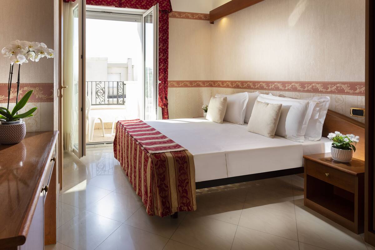 A hotel room with a bed, bedside table, and a potted plant.