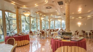 A spacious dining area with round tables covered in red tablecloths, white chairs, and a buffet setup.