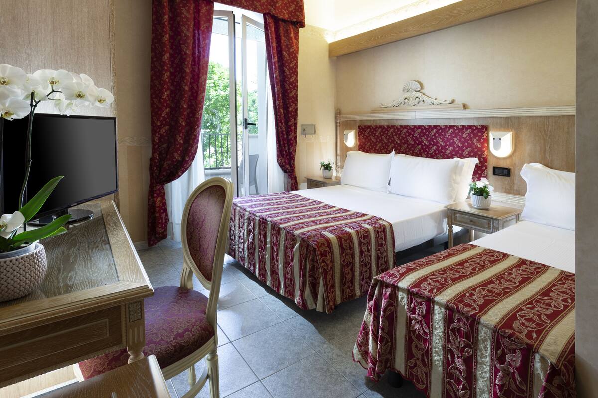 A hotel room with two beds, a desk with a chair, a TV, and a window with curtains.