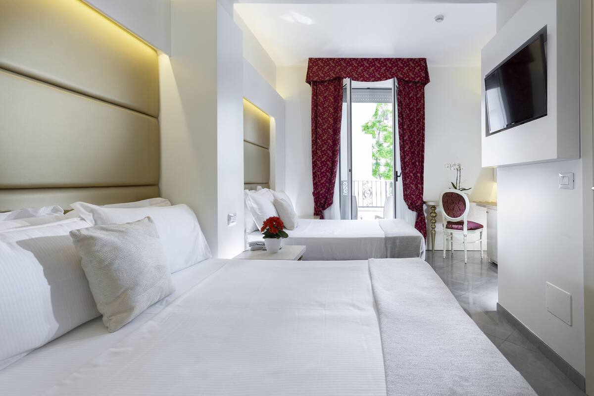 A hotel room with two beds, a TV mounted on the wall, a small table with a vase of flowers, and a chair.