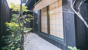 A traditional Japanese building with a wooden exterior, a tiled entrance, and a small garden area with trees and shrubs. - Hotel Zipangu Tameikecho (Kyoto)