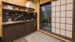 A kitchen with a black tiled backsplash, a built-in stove, and a window with a view of greenery. - Hotel Zipangu Tameikecho (Kyoto)