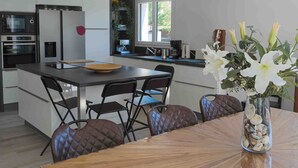 A modern kitchen with a central island, black chairs, and a wooden dining table with a vase of flowers. - Villa with 132 m2 of living space large living area large terrace and landscaped garden (Vias)