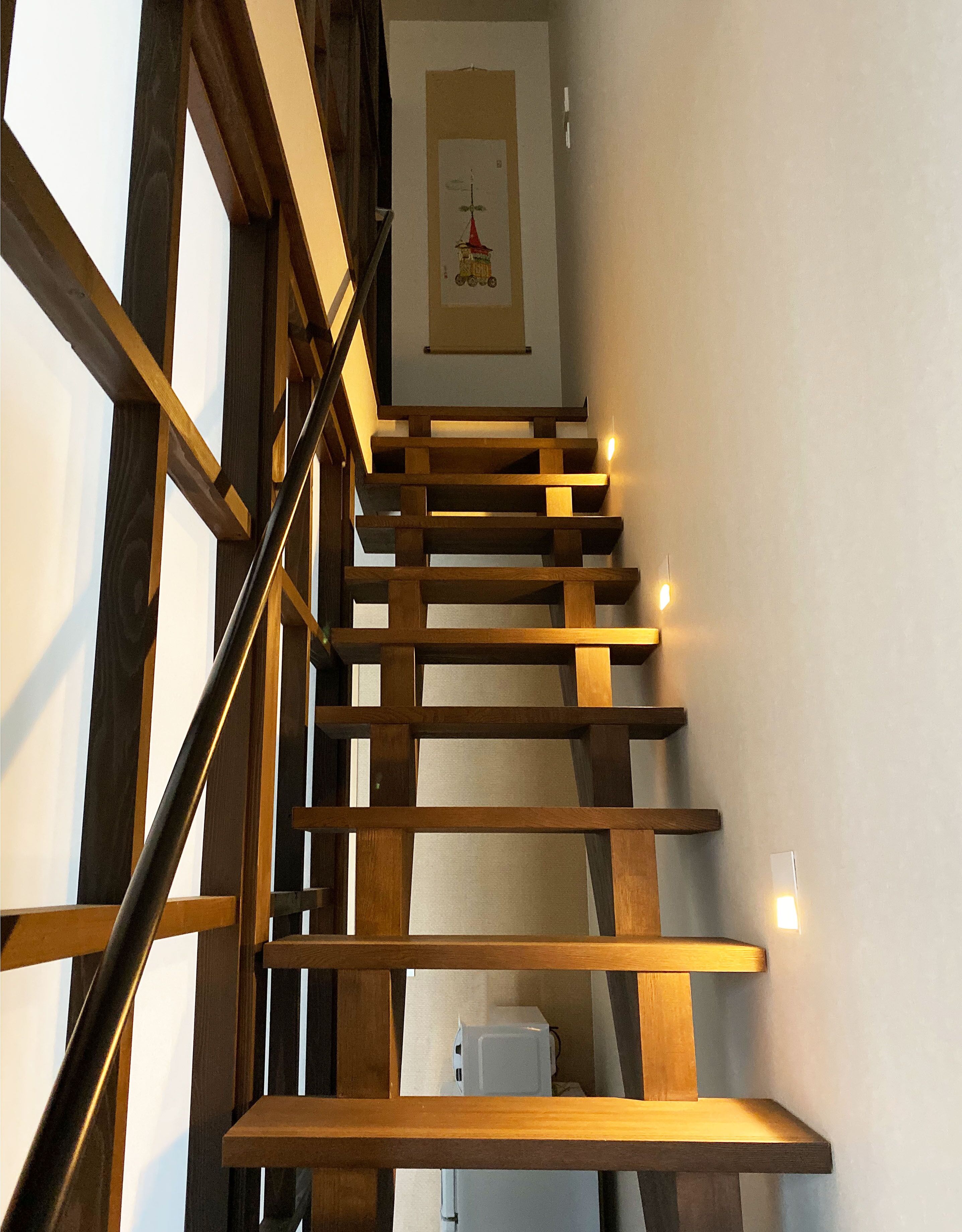 A wooden staircase with a handrail, a white wall with a framed picture, and a white appliance at the bottom.