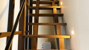 A wooden staircase with a handrail, a white wall with a framed picture, and a white appliance at the bottom. - Hotel Zipangu Murasakino (Kyoto)