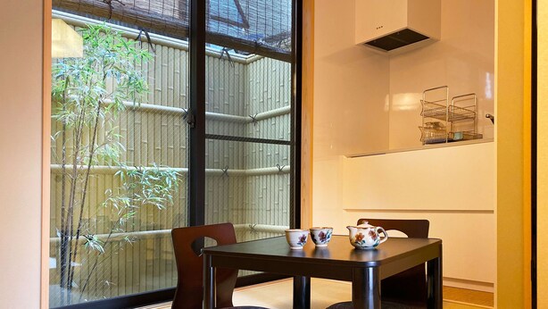 A traditional Japanese-style room with tatami flooring, a low table with a tea set, and a view of bamboo outside. - Hotel Zipangu Murasakino (Kyoto)