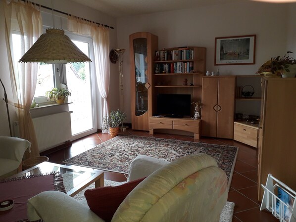 A living room with a sofa, a coffee table, a bookshelf, a television, and a window with curtains.