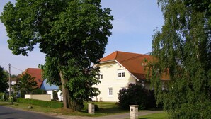 A two-story house with a red-tiled roof, surrounded by lush greenery and a clear sky. - Max Kuehlungsborn House (Kühlungsborn)