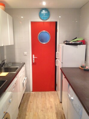 A compact kitchen with white cabinets, a red door, and a small refrigerator.