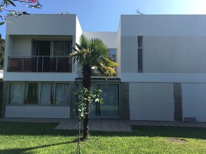 A modern two-story building with large windows and a small palm tree in the front yard.