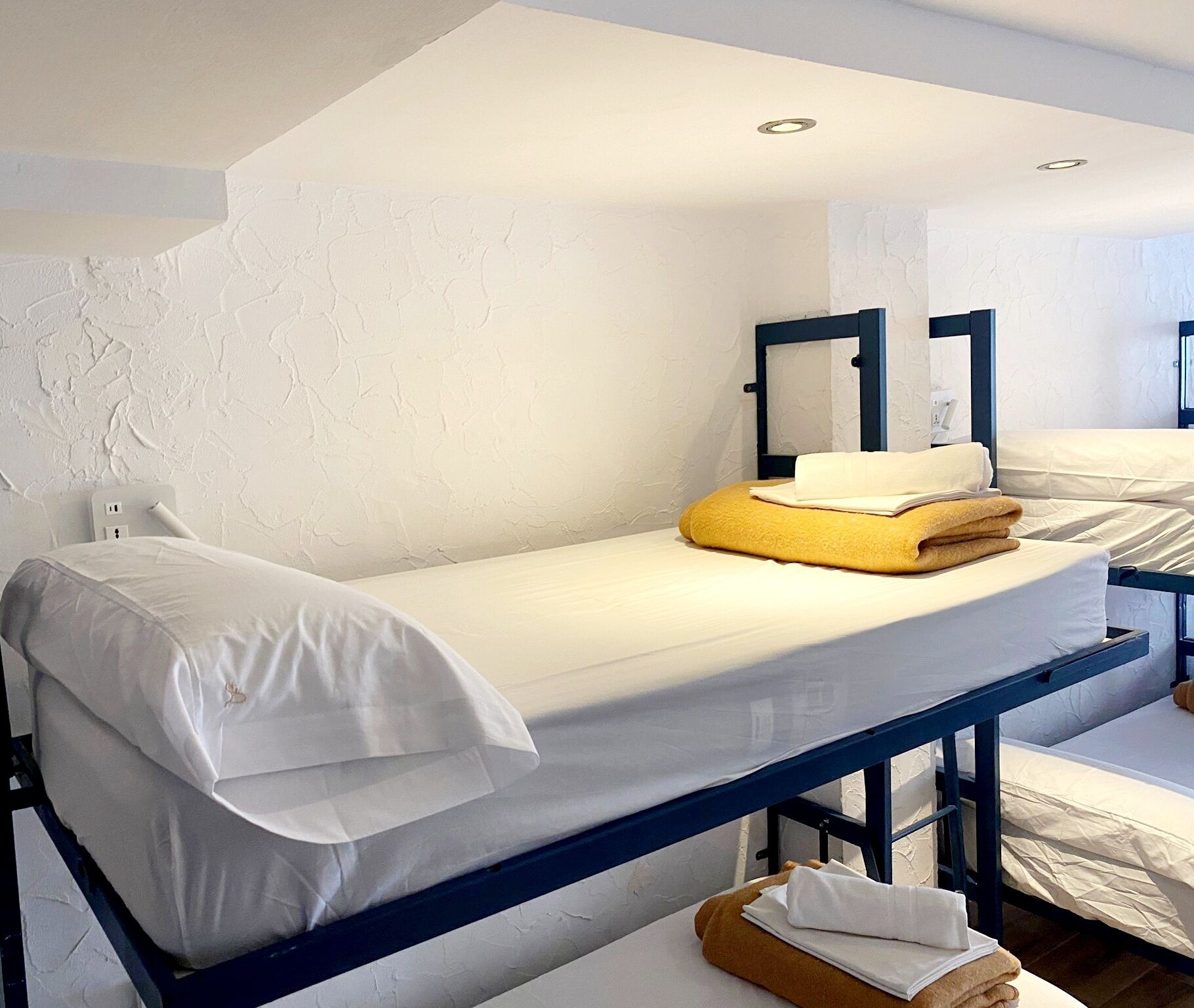 Una cama individual con ropa de cama blanca, una toalla amarilla y una mesita de noche de madera.