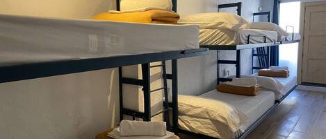 A dormitory-style room with bunk beds, wooden flooring, and a door leading to another room.