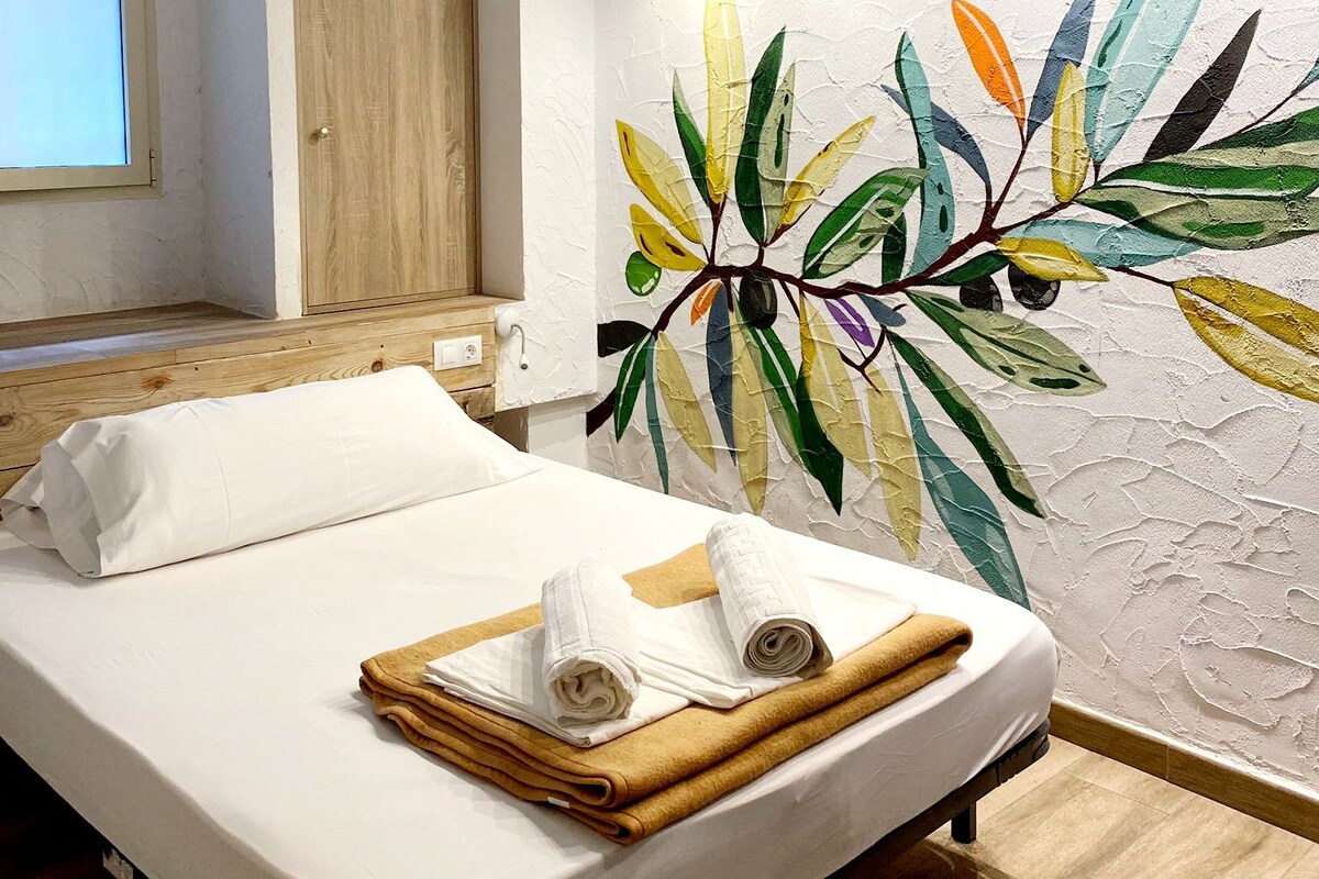 Una habitación de hotel con cama, aire acondicionado en la pared, ventana y puerta de madera.