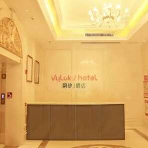 Zona de recepción de un hotel, con un amplio mostrador, una araña de cristal, obras de arte enmarcadas en la pared y un cartel con el nombre del hotel.