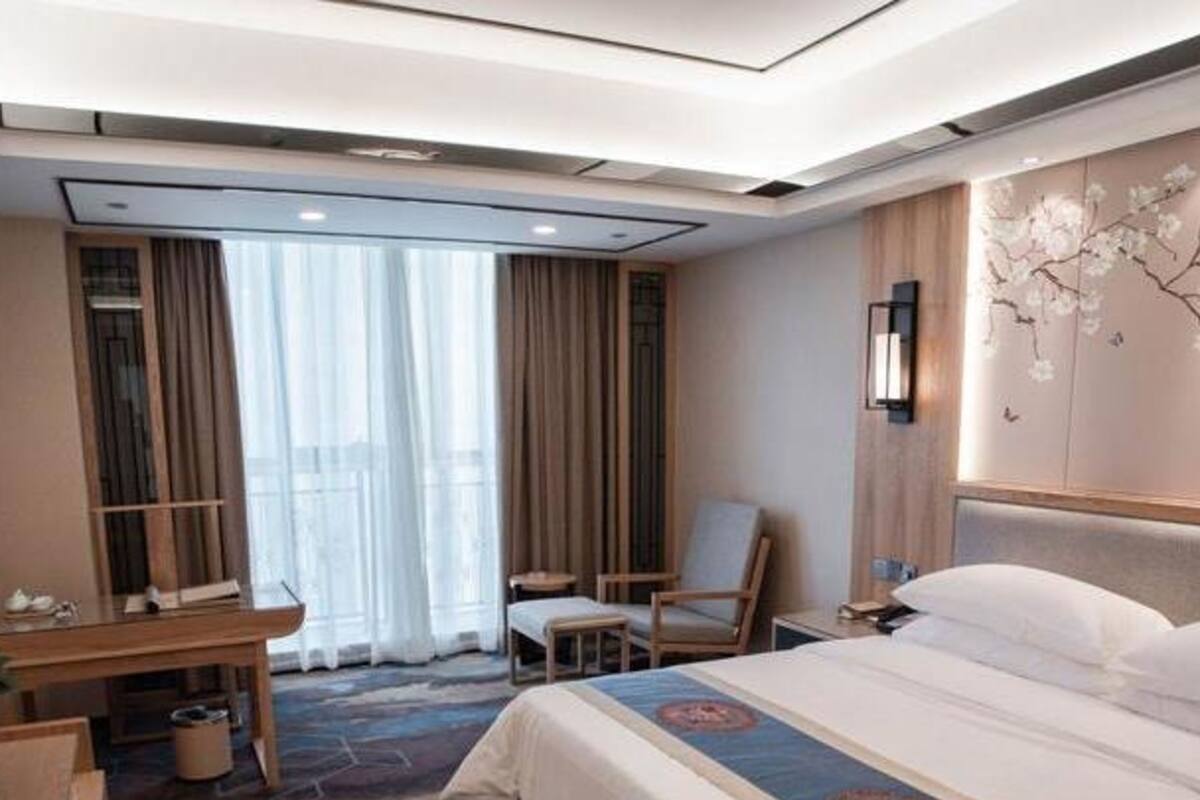 A hotel room with a large bed, a desk, a chair, and a view of the outdoors through the window.